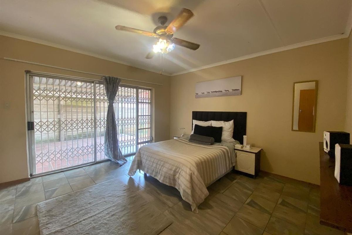 Spacious bedroom featuring tiled flooring, a ceiling fan, and large sliding glass doors with security gates providing direct access to the outdoor patio area.