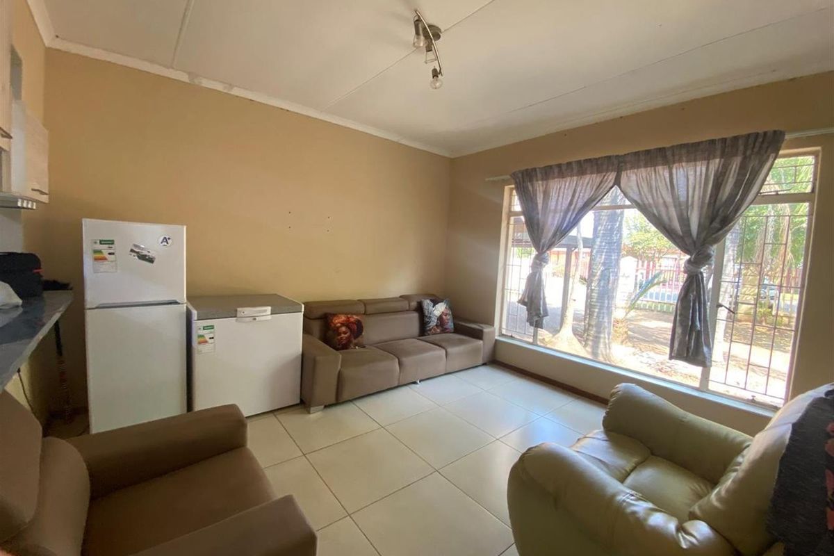 A living room area featuring large windows with natural light, tiled flooring, and direct access to the exterior.