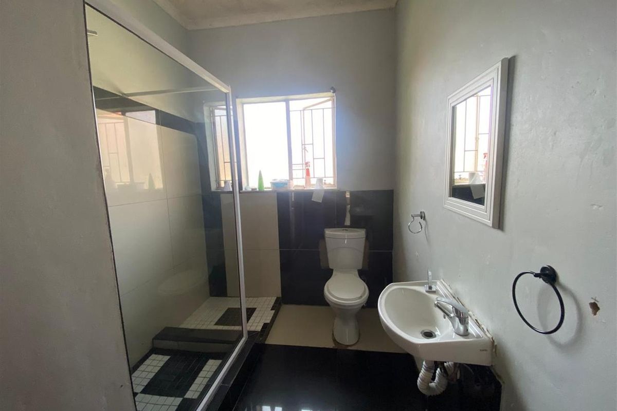 A functional bathroom featuring a glass-enclosed shower, a pedestal sink, and a toilet, with black and white tiled flooring and wall accents.