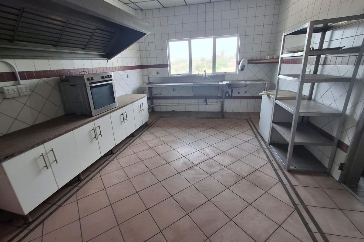 Commercial kitchen featuring tiled walls, stainless steel sink, built-in oven, large extractor hood, and ample floor space for food preparation.