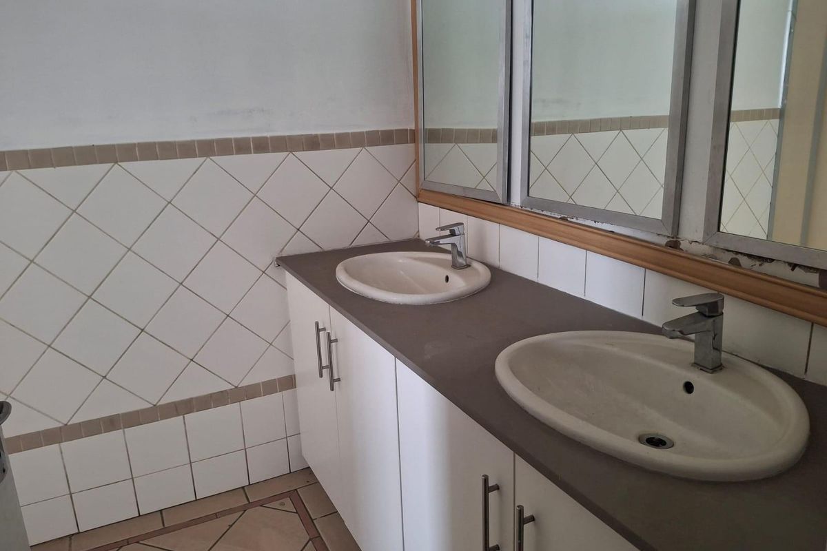 A functional bathroom vanity area featuring a double basin setup with white cabinetry, tiled walls, and a large wall-mounted mirror.
