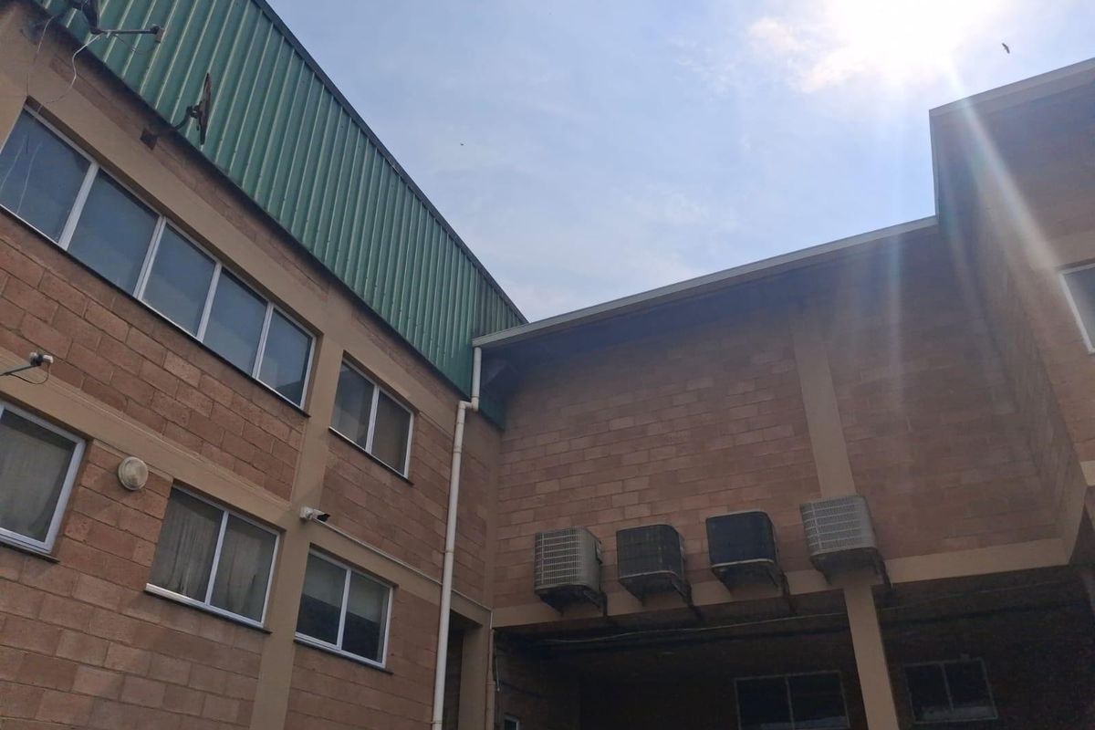 Exterior view of a commercial building featuring face brick facade, metal roof cladding, and multiple wall-mounted air conditioning condenser units.
