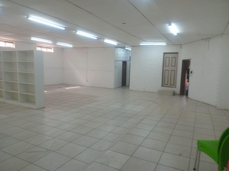 Spacious open-plan commercial area featuring tiled flooring, painted brick walls, and built-in shelving, suitable for retail or office use.