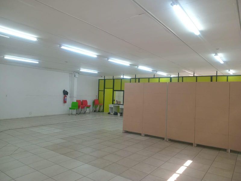 A large, open-plan commercial space featuring tiled flooring, fluorescent lighting, and modular partition walls, suitable for various business or office configurations.