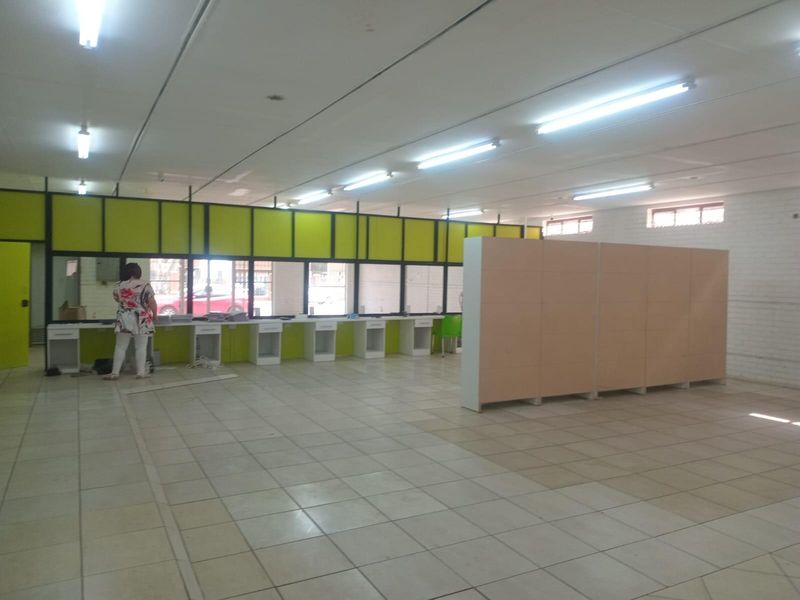 Open-plan commercial office space featuring tiled flooring, built-in service counters, and fluorescent lighting, suitable for various business operations.