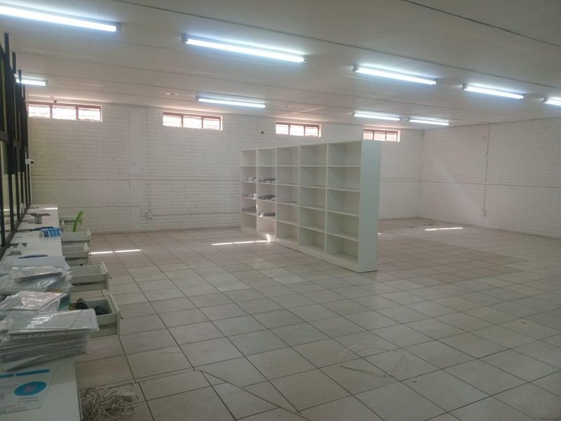 Spacious open-plan commercial area featuring tiled flooring, exposed brick walls, high-level windows, and integrated shelving units, suitable for office or retail use.