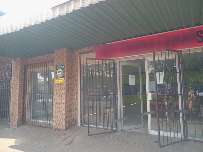 Commercial storefront entrance featuring a brick facade, metal awning, and security gates over glass doors.