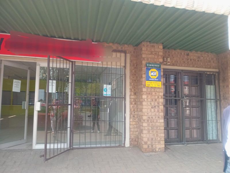 Commercial storefront featuring a brick facade, glass entrance doors, and security gates under a corrugated metal awning.