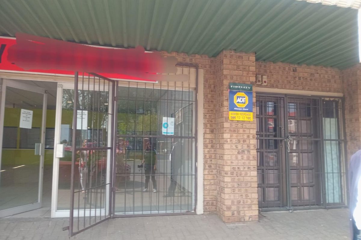 Commercial storefront featuring a brick facade, glass entrance doors, and security gates under a corrugated metal awning.