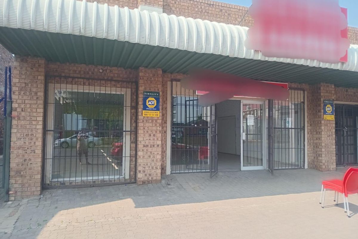 Commercial storefront featuring a face brick facade, corrugated metal awning, and secure metal gates over glass display windows.