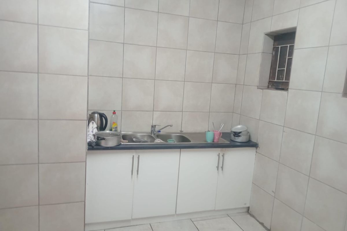 A compact kitchen area featuring base cabinetry, a double basin sink with mixer tap, and full-height wall tiling.