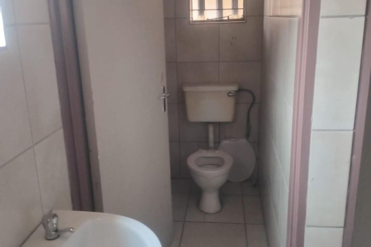 A compact bathroom featuring a pedestal basin, toilet, and tiled finishes with security bars on the window.