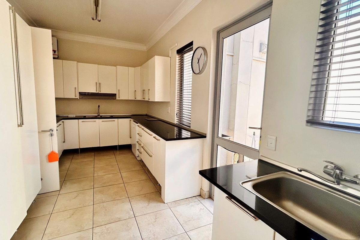 Modern kitchen featuring white cabinetry, contrasting black countertops, tiled flooring, and a stainless steel sink with direct access to an outdoor area.