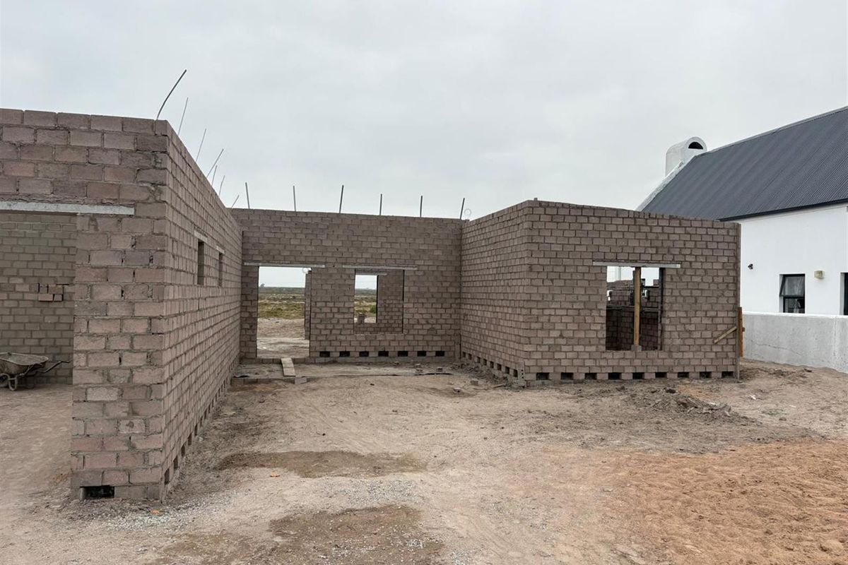 A view of a property under construction, featuring exposed concrete block walls and structural openings for future doors and windows.