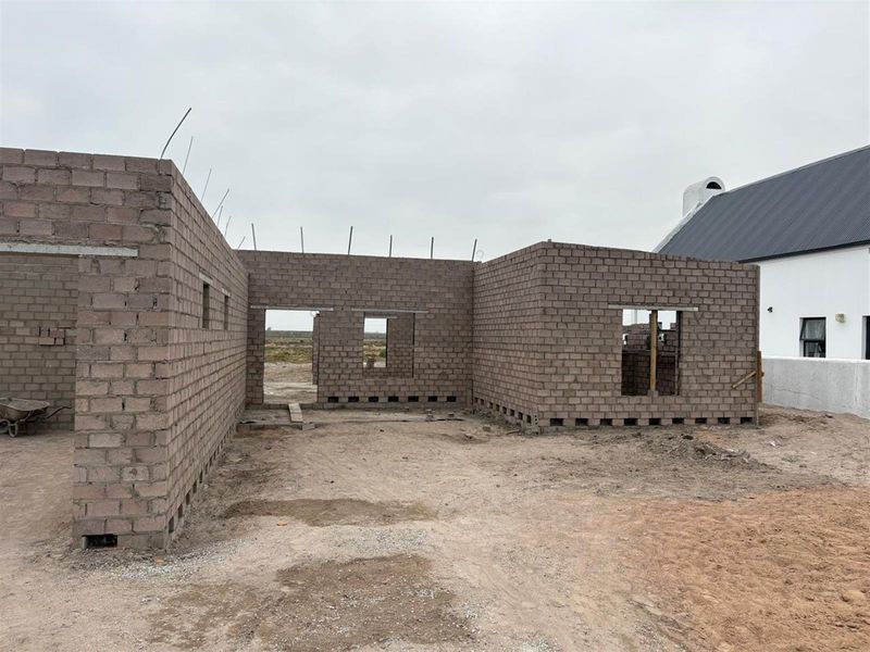 A view of a property under construction, featuring exposed concrete block walls and structural openings for future doors and windows.