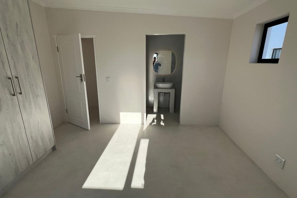 A clean, modern bedroom featuring built-in wardrobes, smooth flooring, and an en-suite vanity area with a basin and mirror.
