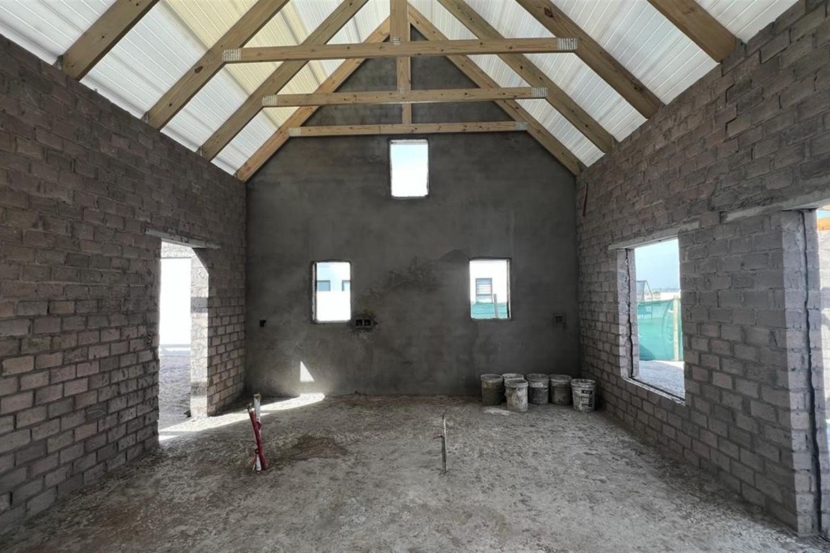 An unfinished interior space featuring exposed brick walls, timber roof trusses, and cement flooring, offering a blank canvas for custom interior design and completion.