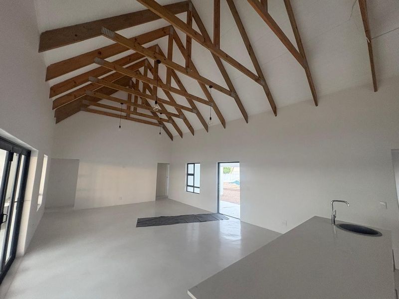 Spacious open-plan living area featuring a high vaulted ceiling with exposed timber trusses, polished concrete floors, and a modern kitchen island.