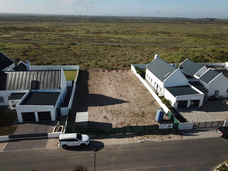 Aerial view of a vacant residential plot situated between two established modern homes in a coastal estate setting.