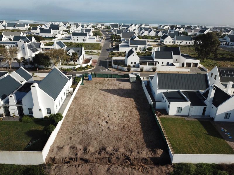 Aerial view of a vacant residential plot situated within a coastal estate, surrounded by established white-walled homes and paved street access.