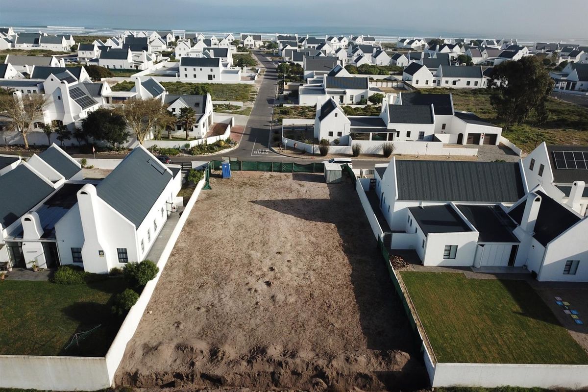 Aerial view of a vacant residential plot situated within a coastal estate, surrounded by established white-walled homes and paved street access.