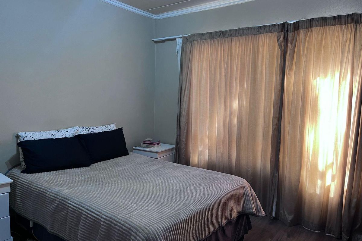 A bedroom featuring laminate flooring, crown molding, and large window treatments allowing natural light into the space.