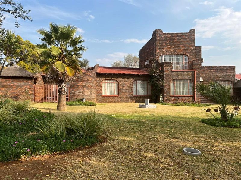 A view of the rear elevation of a multi-level face-brick house featuring a large garden, established landscaping, and a balcony.