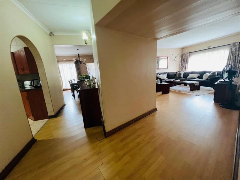 An open-plan living and dining area featuring laminate flooring, an arched entryway to the kitchen, and neutral wall finishes.