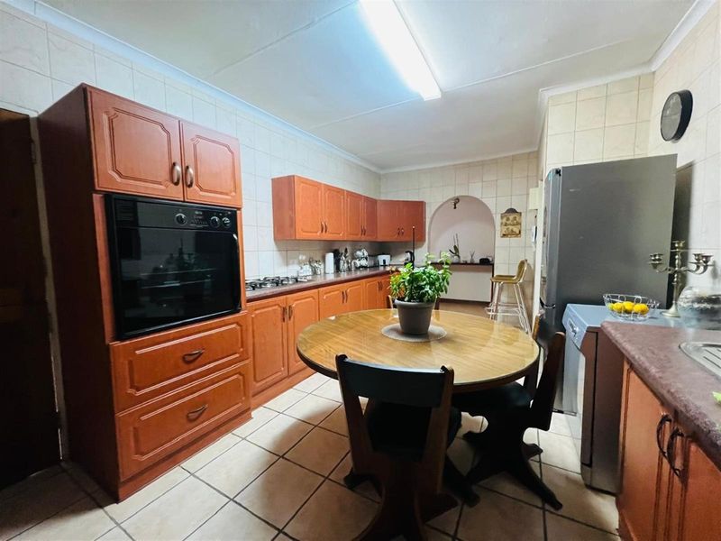 A functional kitchen featuring wooden cabinetry, built-in oven, gas hob, and tiled flooring with an integrated dining area.