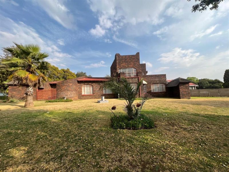 A view of the rear elevation of a face-brick house featuring a multi-level design, set within a spacious garden area.