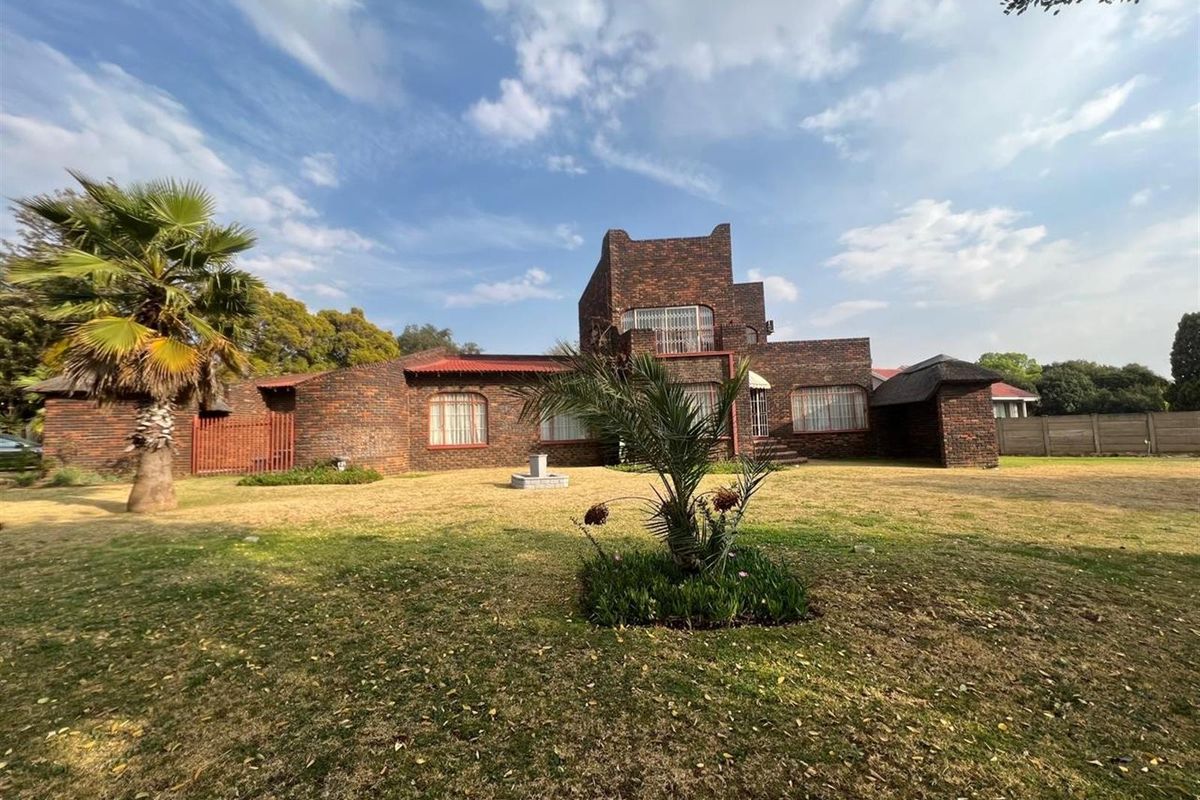 A view of the rear elevation of a face-brick house featuring a multi-level design, set within a spacious garden area.