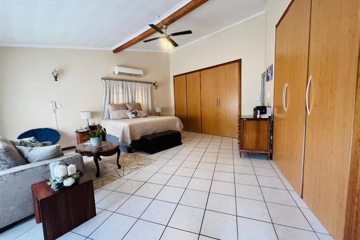 Spacious bedroom featuring tiled flooring, built-in wooden cabinetry, exposed ceiling beams, and a wall-mounted air conditioning unit.