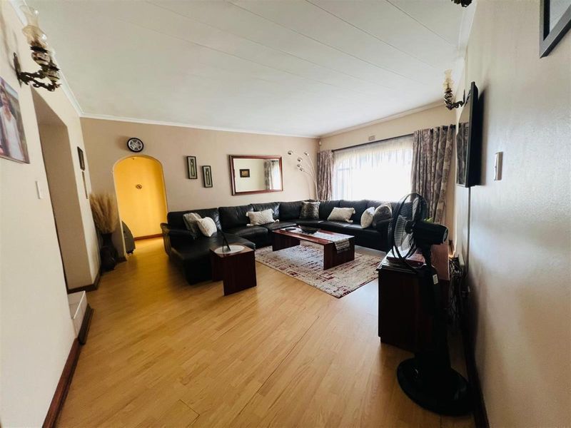 A spacious living room featuring light wood-look flooring, an arched doorway, and large windows allowing for natural light.