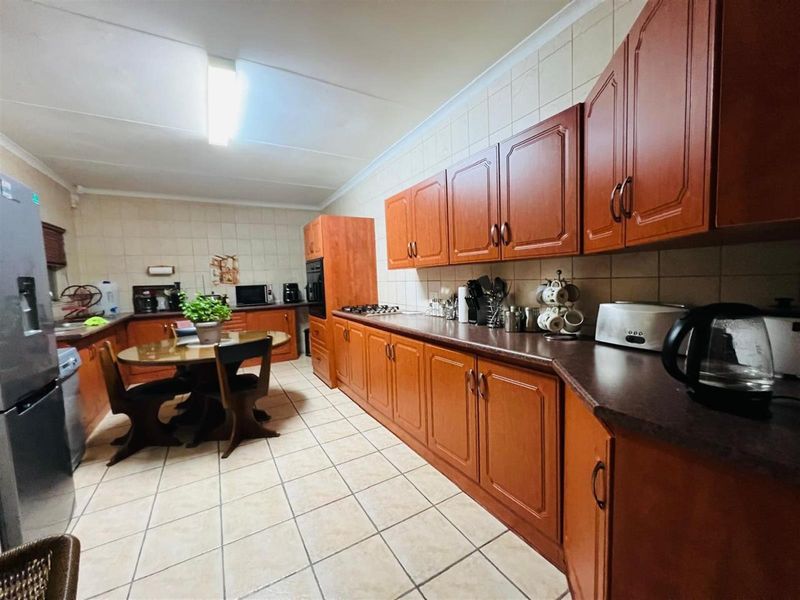 A functional kitchen featuring wooden cabinetry, tiled flooring, and a built-in oven and hob, offering ample counter space and a dedicated dining area.