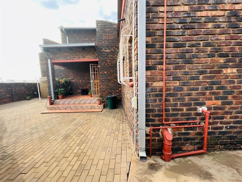 A paved rear courtyard area featuring face-brick exterior walls, a covered patio entrance, and exposed exterior plumbing infrastructure.