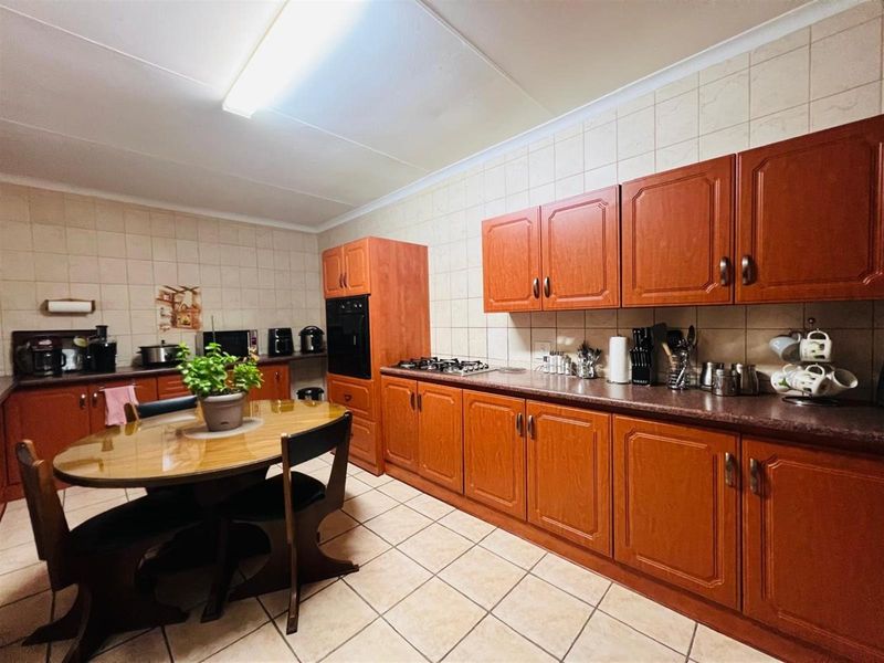 A functional kitchen featuring wood-finish cabinetry, tiled splashbacks, built-in oven, and gas hob, with ample space for a dining table.
