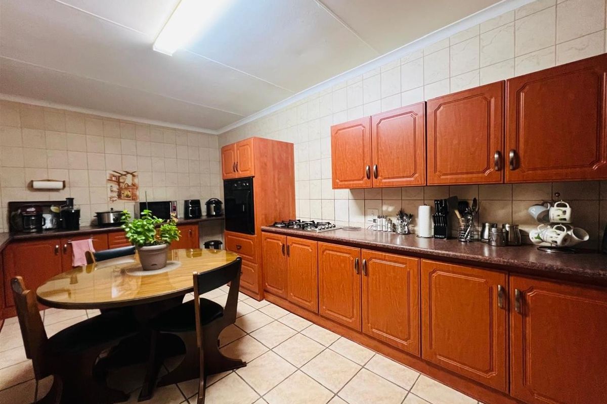 A functional kitchen featuring wood-finish cabinetry, tiled splashbacks, built-in oven, and gas hob, with ample space for a dining table.
