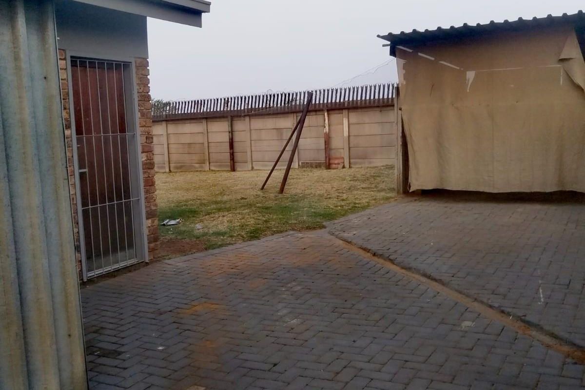 Rear exterior area featuring paved ground, a brick and metal structure, and a perimeter wall with security spikes.