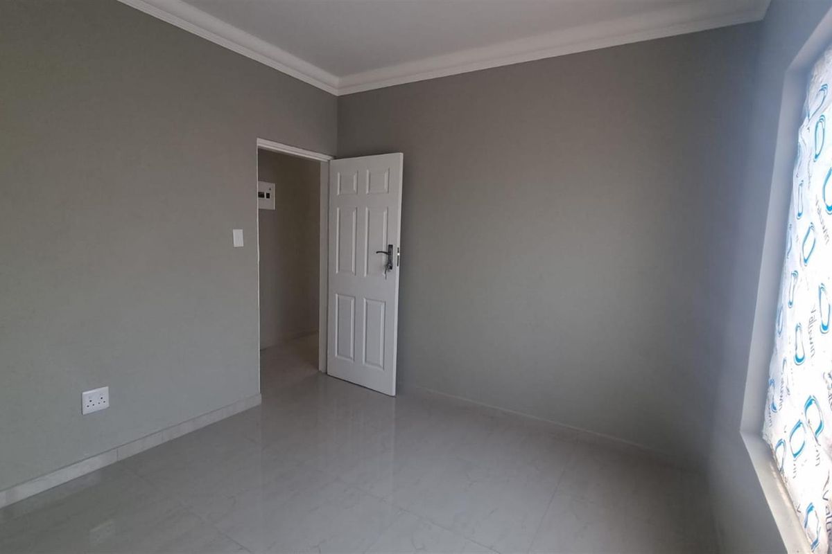 A clean, empty bedroom featuring neutral grey walls, tiled flooring, and a white panel door leading to an adjacent space.