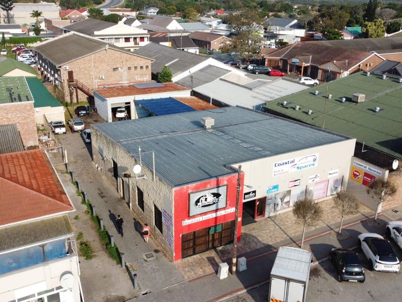 Aerial view of a commercial property featuring a metal roof structure, street-level storefronts, and adjacent parking in a busy urban business district.