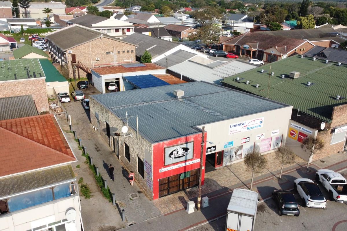 Aerial view of a commercial property featuring a metal roof structure, street-level storefronts, and adjacent parking in a busy urban business district.