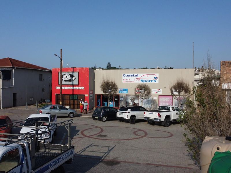 Commercial retail strip featuring multiple storefronts with signage, paved parking area, and street-level access in a busy commercial zone.
