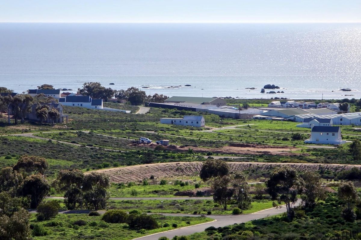 An elevated aerial view overlooking a coastal landscape with scattered residential buildings, natural vegetation, and a clear view of the ocean.