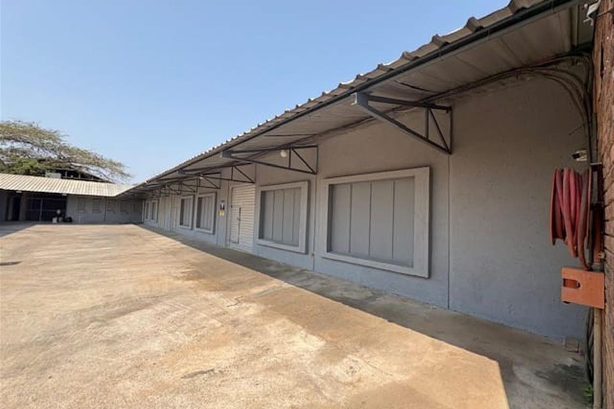 Exterior view of an industrial warehouse facility featuring a large concrete yard, metal roof overhang, and secure window shutters.