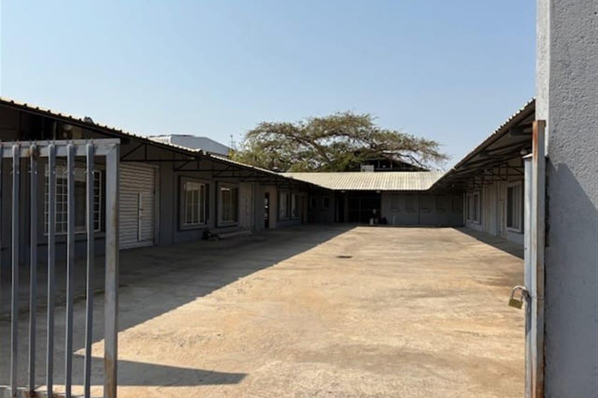 A spacious industrial courtyard featuring concrete paving, surrounded by functional warehouse units with metal roofing and secure gated access.