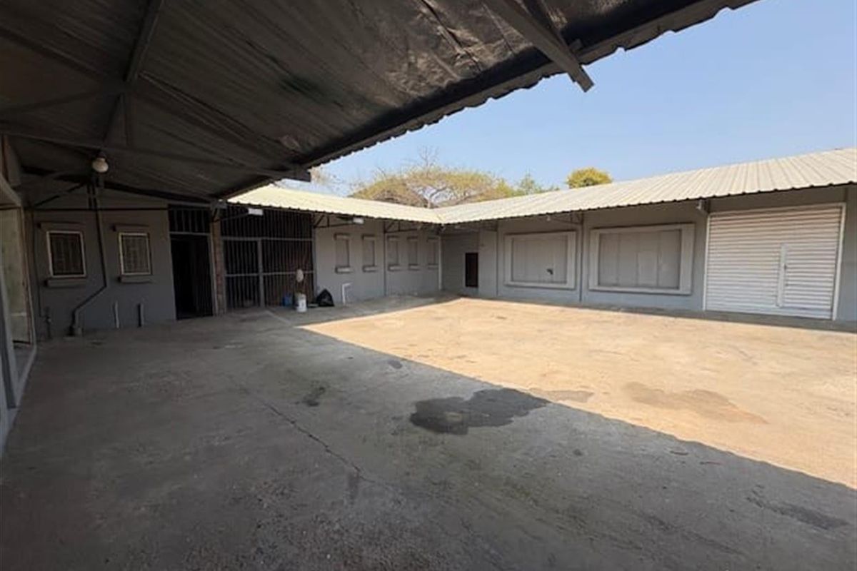Spacious industrial courtyard featuring a large concrete yard, covered loading area, and secure metal roller shutter doors.