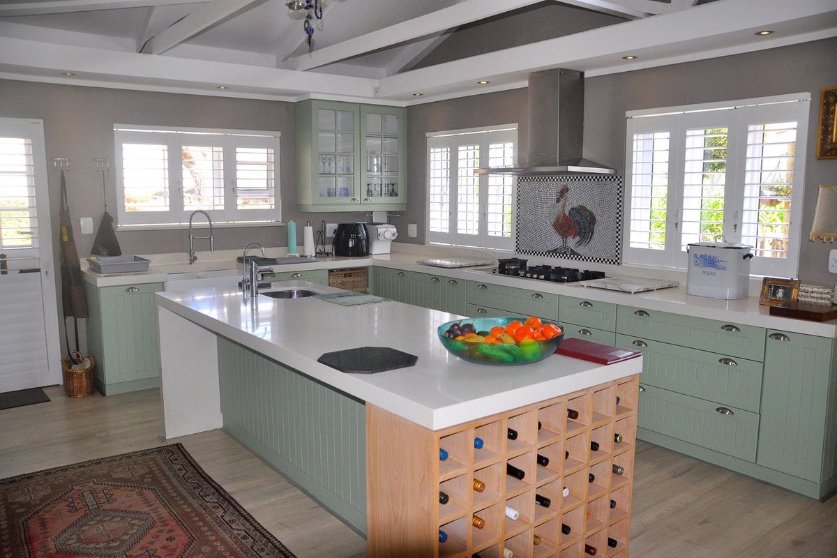 Spacious kitchen featuring a large central island with integrated wine storage, stone countertops, shaker-style cabinetry, and a stainless steel extractor fan.