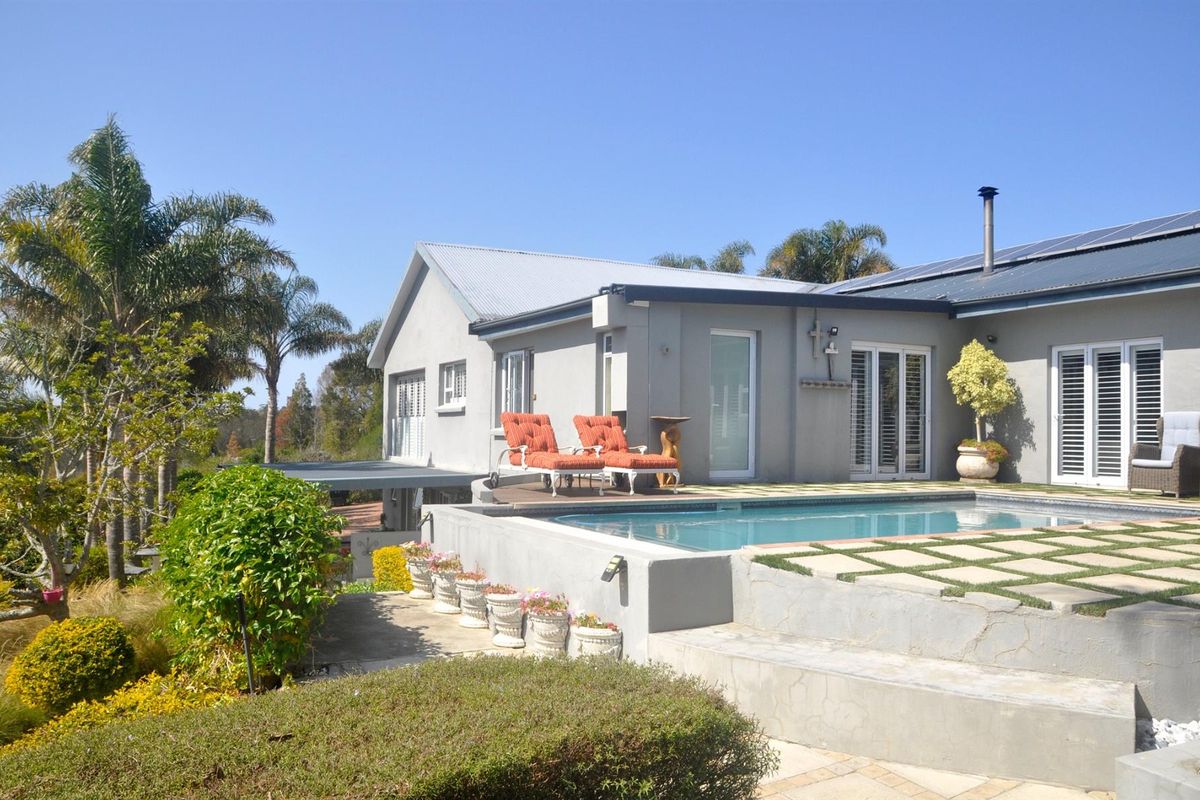 Rear view of the property featuring a raised swimming pool, paved patio area, and landscaped garden with established trees.