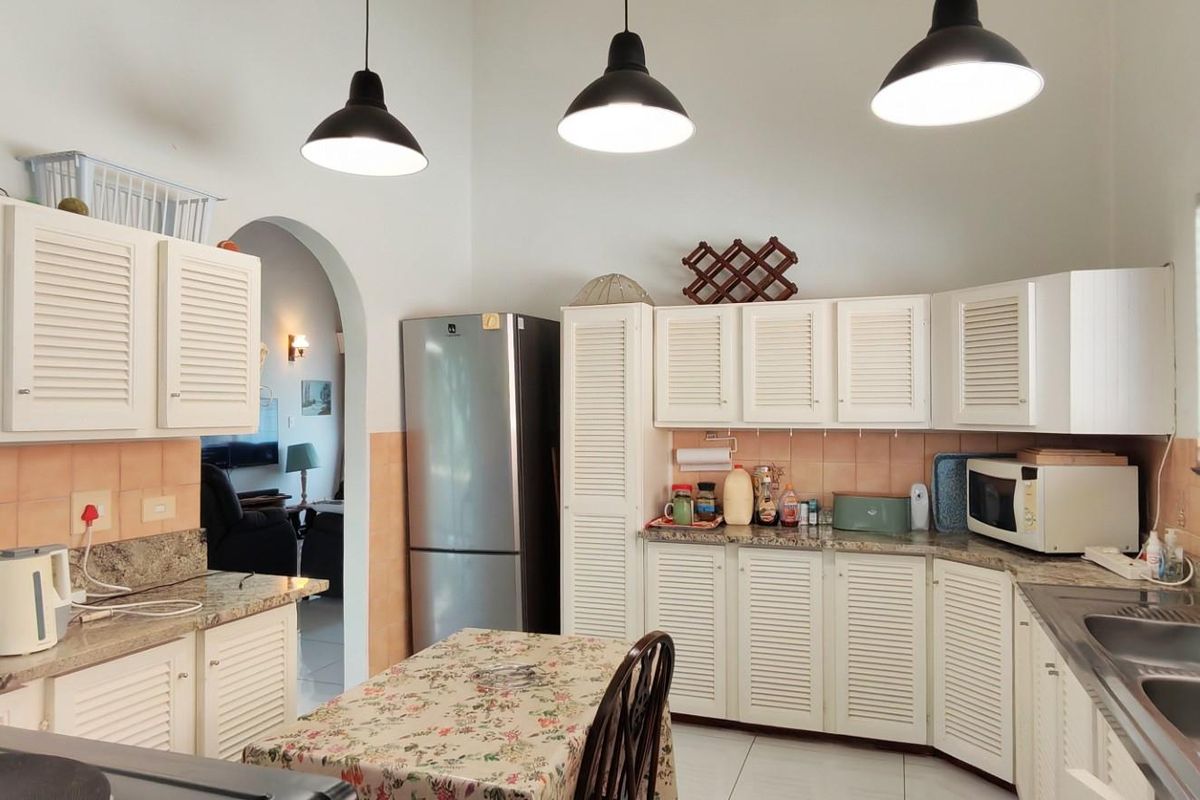 A functional kitchen featuring white louvered cabinetry, granite countertops, a double stainless steel sink, and pendant lighting, with an arched entryway to the living area.