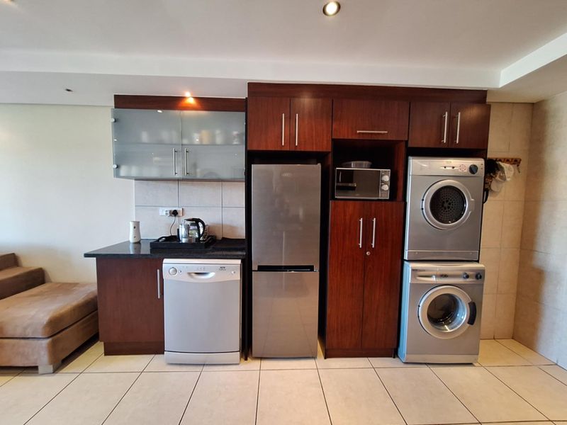 A compact kitchen area featuring dark wood cabinetry, granite countertops, tiled backsplash, and integrated appliance housing for a dishwasher, fridge, and laundry units.